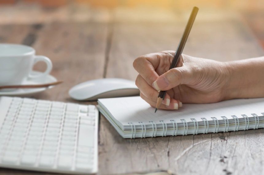 A person writing in a notebook next to a keyboard.